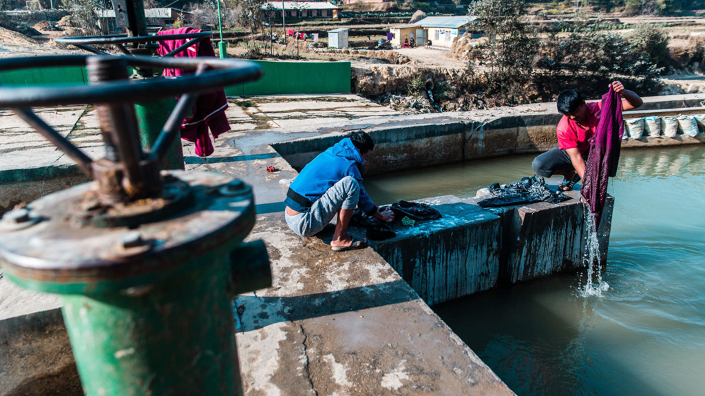 Two Nepali men wash clothes on a canal just downstream of a hydroelectric dam. Photo: Pramin Manandhar