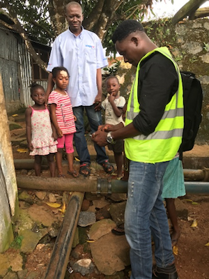 A family looks on as technician Dennis Koroma maps water pipes in Freetown, Sierra Leone. Waterborne diseases are a pressing problem, exacerbated by poor infrastructure, including broken pipes. MCC’s investments support the Government of Sierra Leone in its efforts to strengthen Freetown’s water utility.
